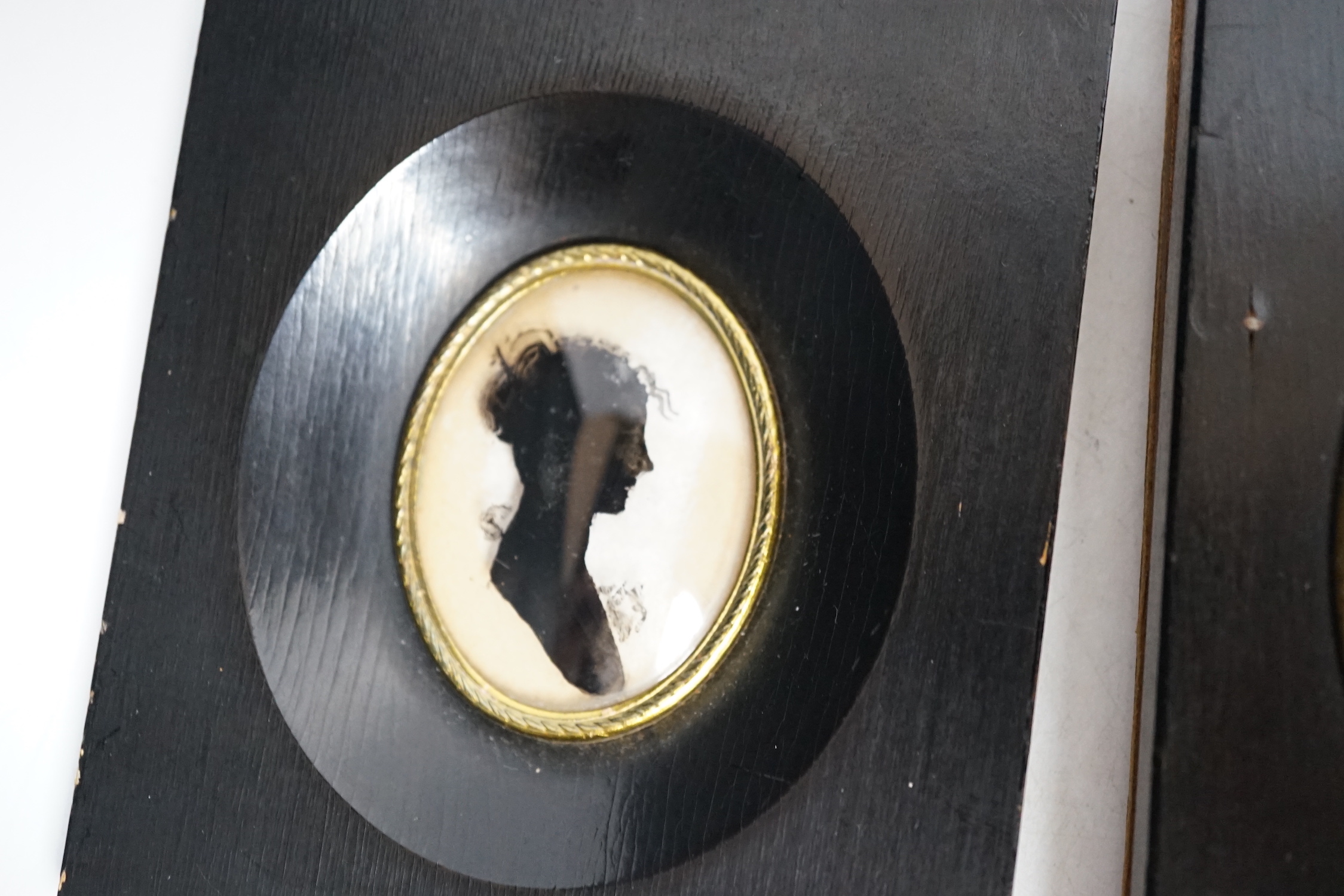 Three miniature reverse glass painted silhouettes, a relief plaque of the virgin and child and a watercolour portrait pendant